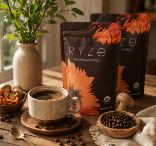 Two bags of RYZE Mushroom Coffee on a rustic wooden table, styled with a cup of coffee, bowls of mushrooms and coffee beans, and a potted plant in the background.