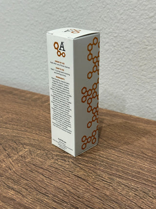 A tall white rectangular product box with orange circular honeycomb-style graphics and printed text, standing on a wooden tabletop against a light textured wall.