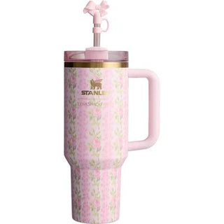A pink Stanley tumbler with a floral pattern, featuring a built-in handle, a pink lid, and a matching pink straw with a bow on a white background.